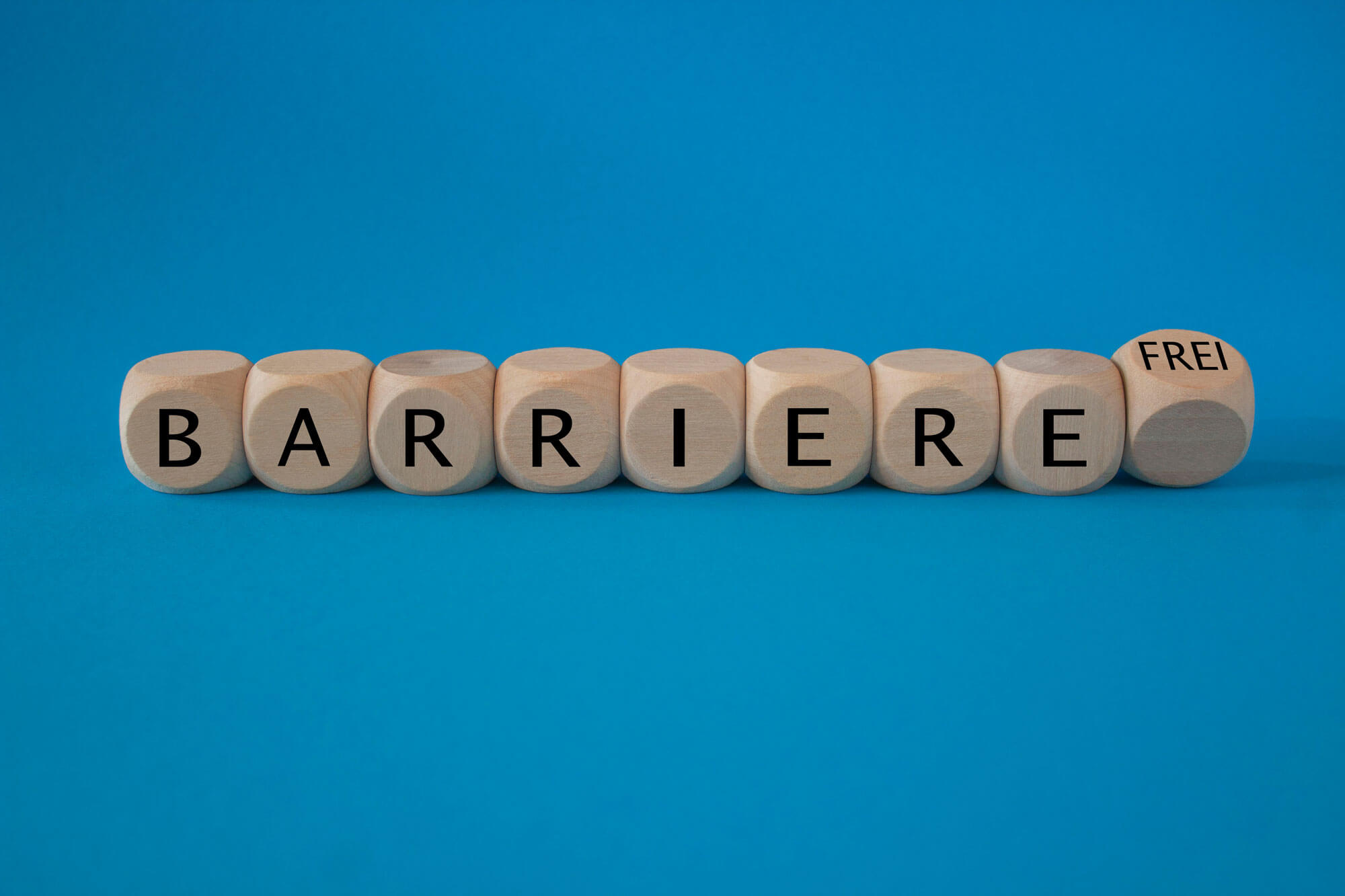 Holzwürfel mit den Buchstaben BARRIERE und FREI auf blauem Hintergrund
