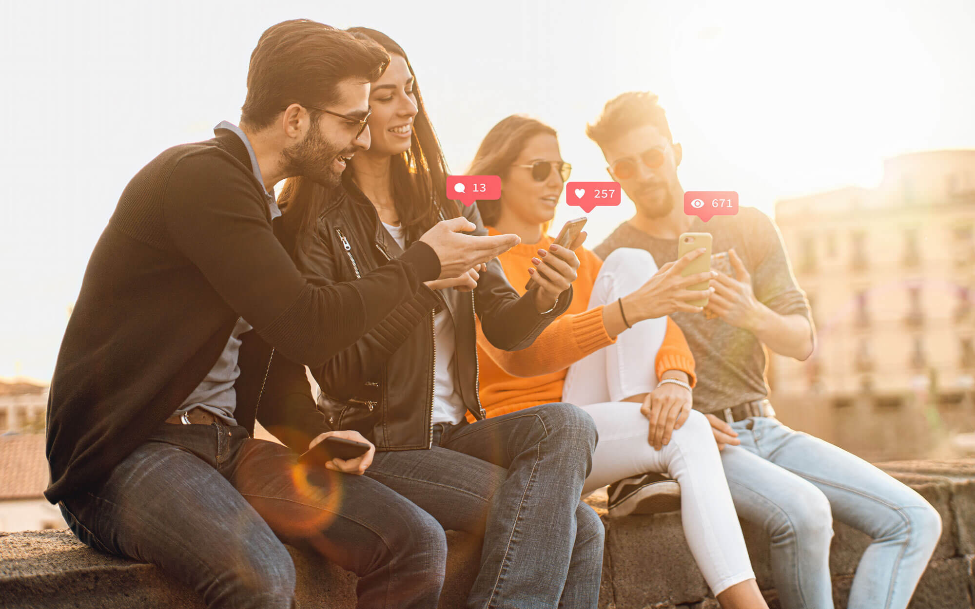Vier junge Leute sitzen draußen und schauen auf ein Smartphone, das eine Frau hält