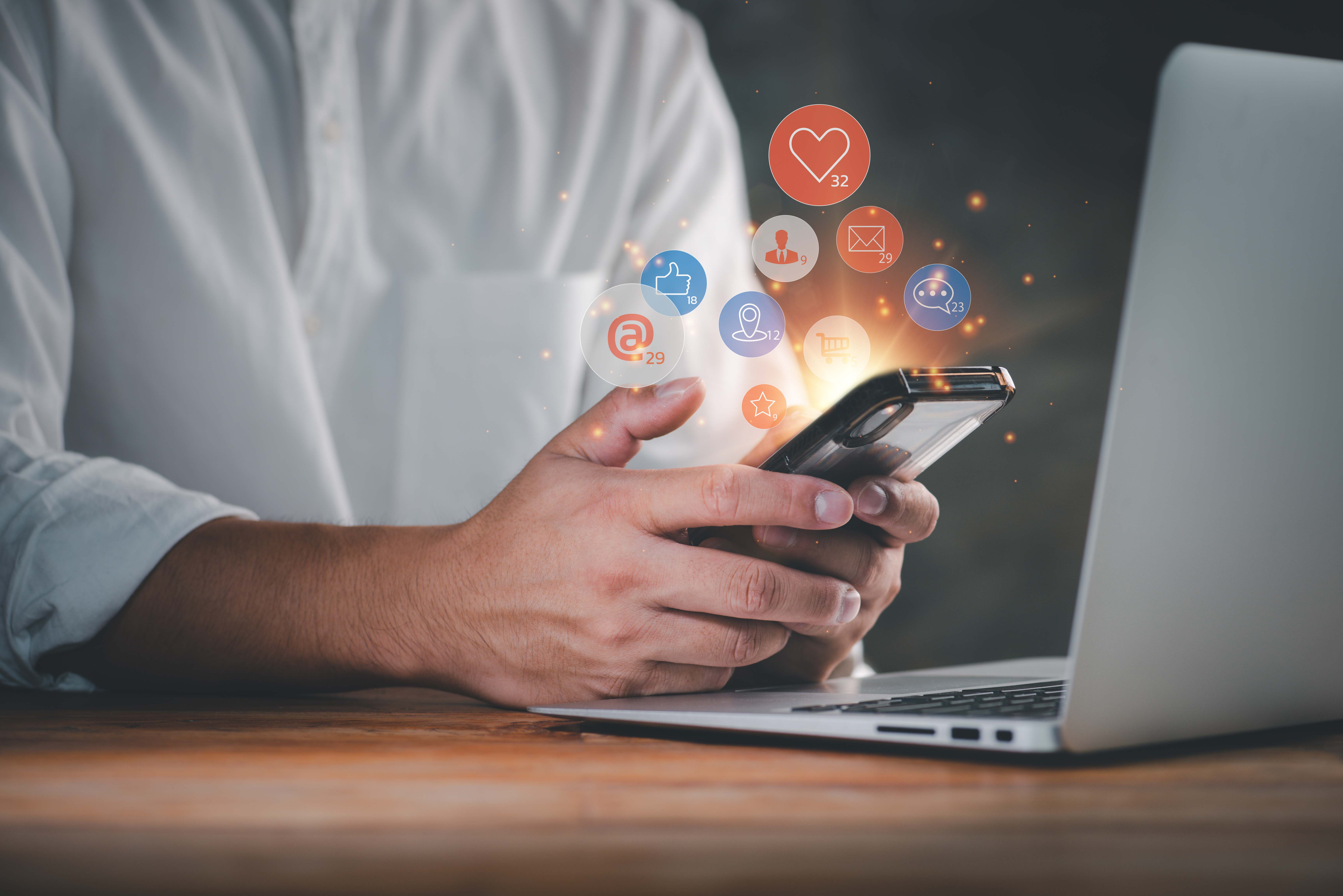 Person hält ein Smartphone in der Hand, über dem verschiedene Social-Media-Icons schweben